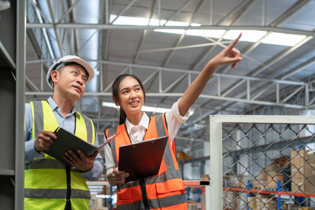 Young female inventory worker and male supervisor point to products on shelves at warehouse factory